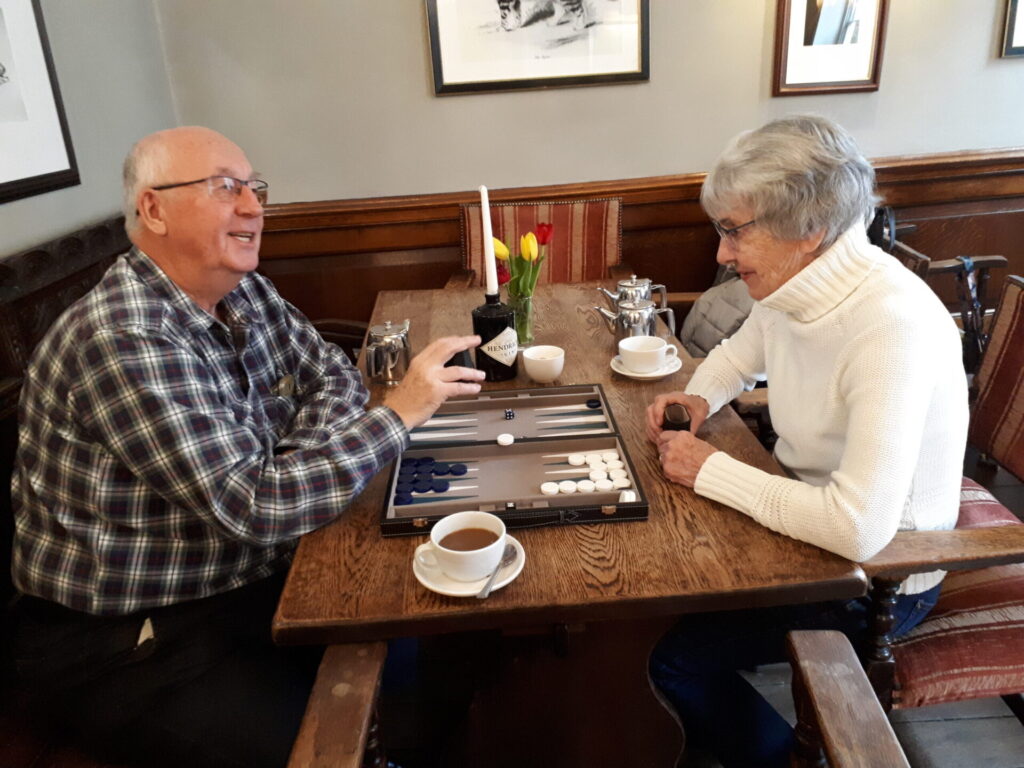 Photo of two people playing Backgammon in a pub with cups of coffee on the table